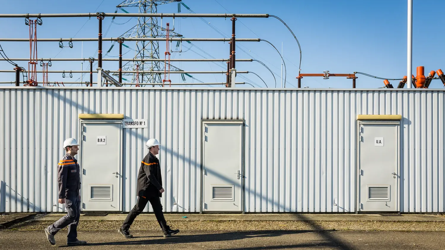 Two engineers with helmets walking past electricity station